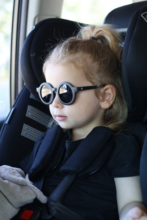 Toddler in a car seat, wearing black Hey Peeps Roundabouts sunglasses