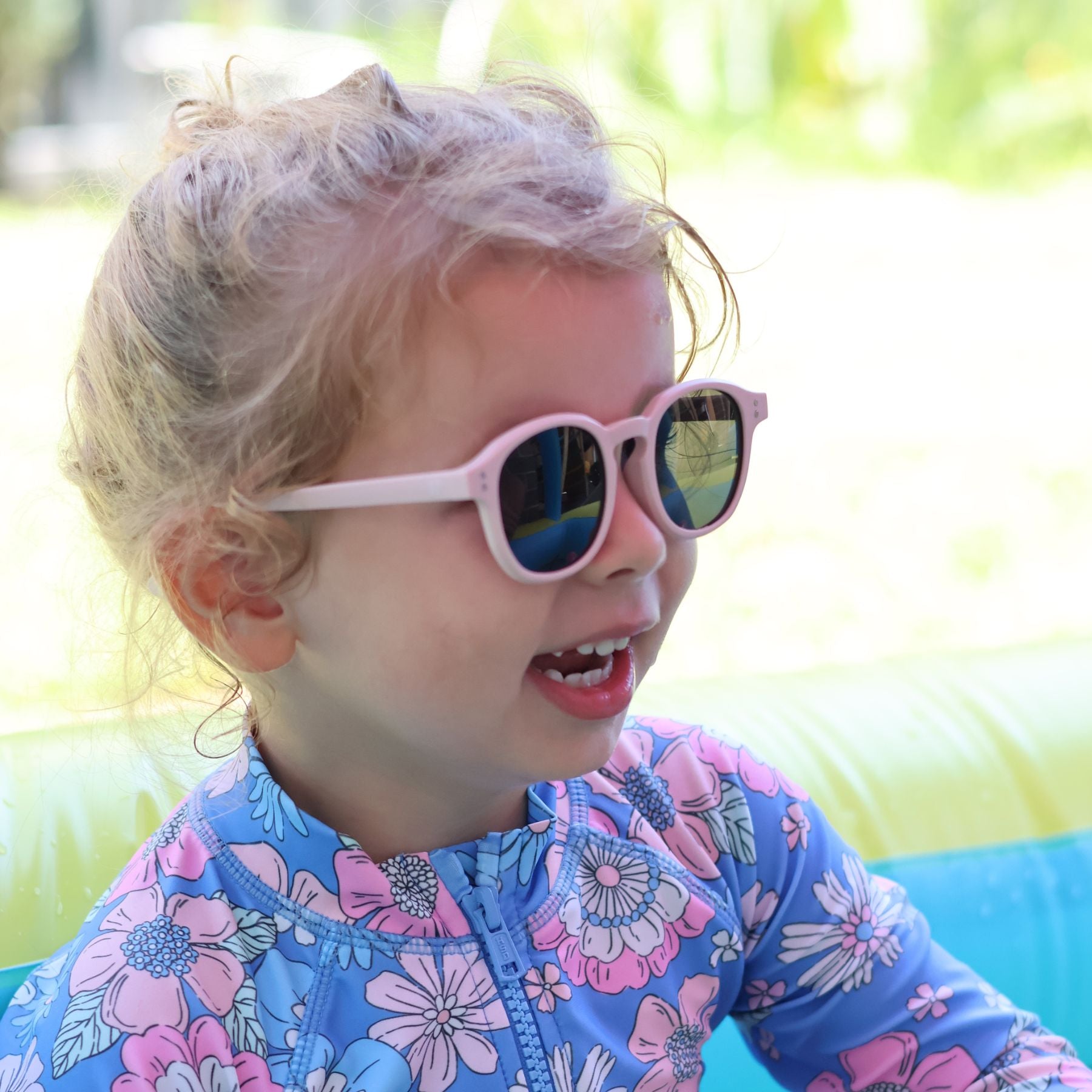 A toddler in pink sunglasses and a floral swim top, mid laugh